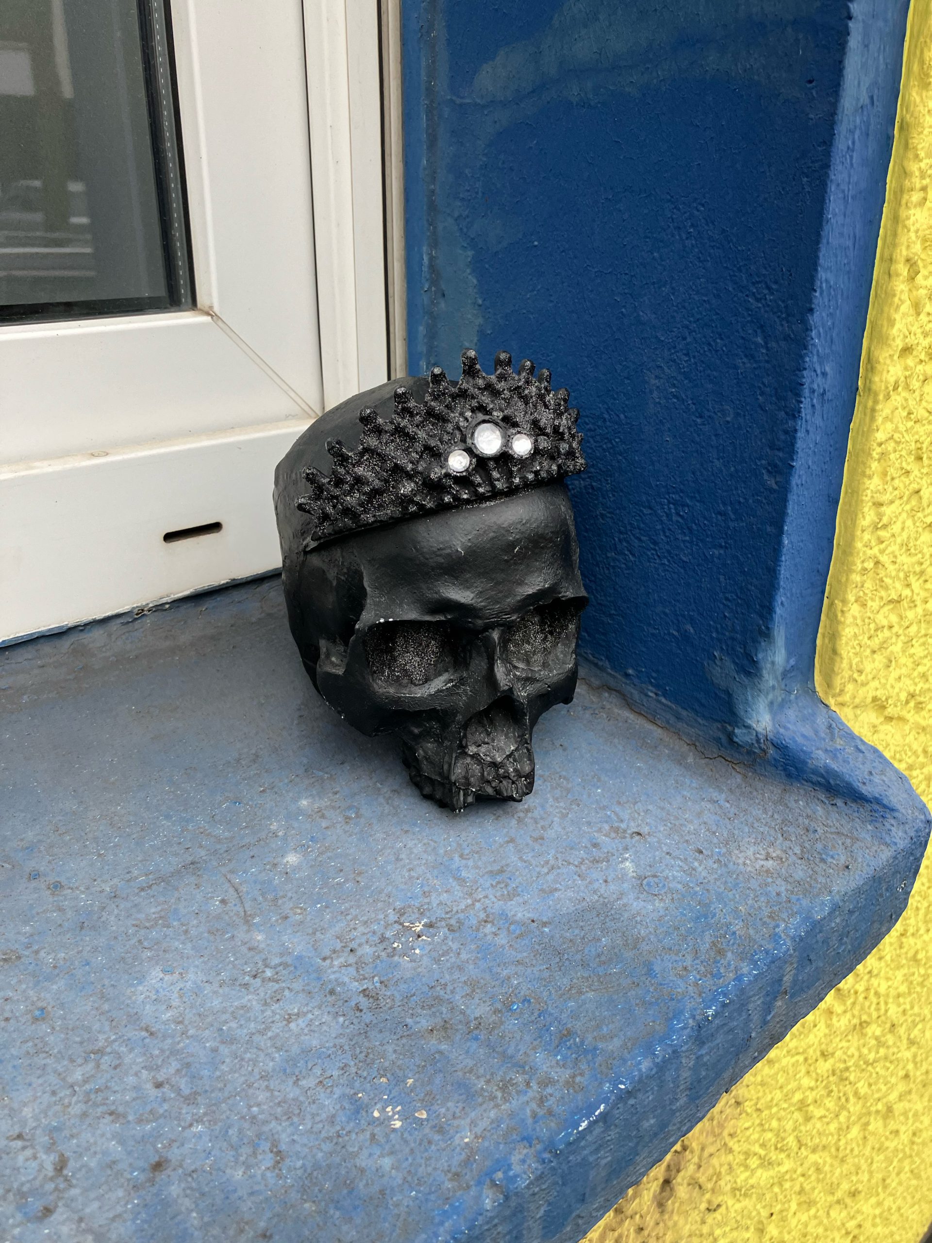 Ein schwarzer Kunststoffschädel mit Diadem auf einem Fensterbrett. 