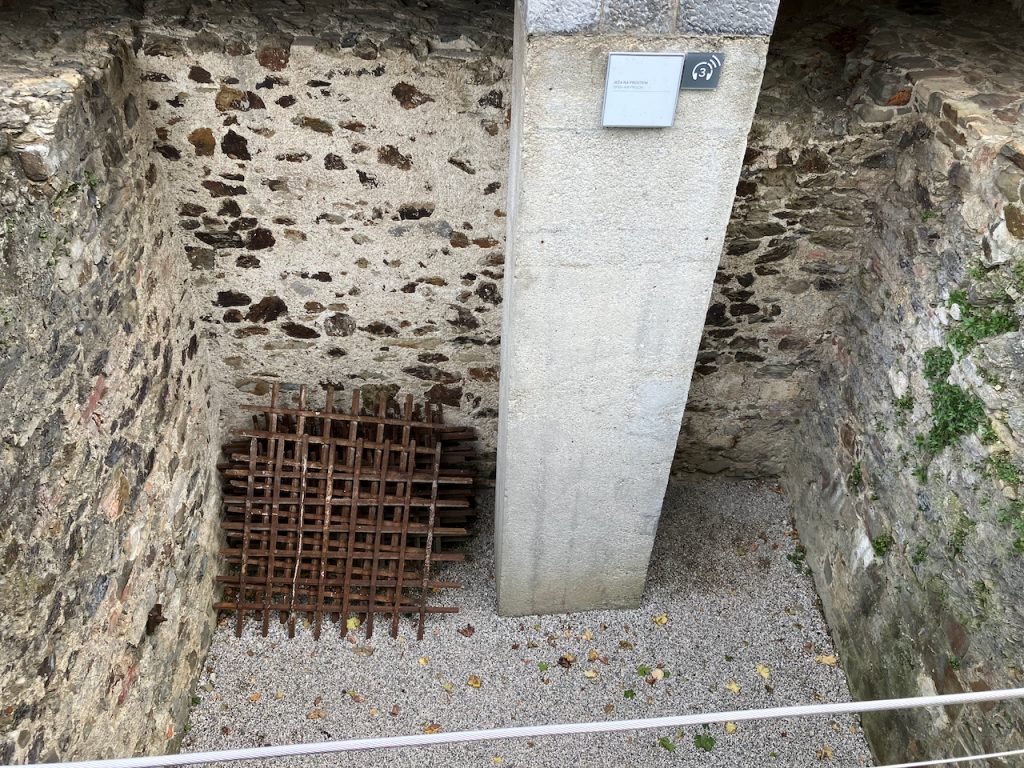 Blick in eine gemauerte Grube. An die Wand gelehnt Metallgitter.