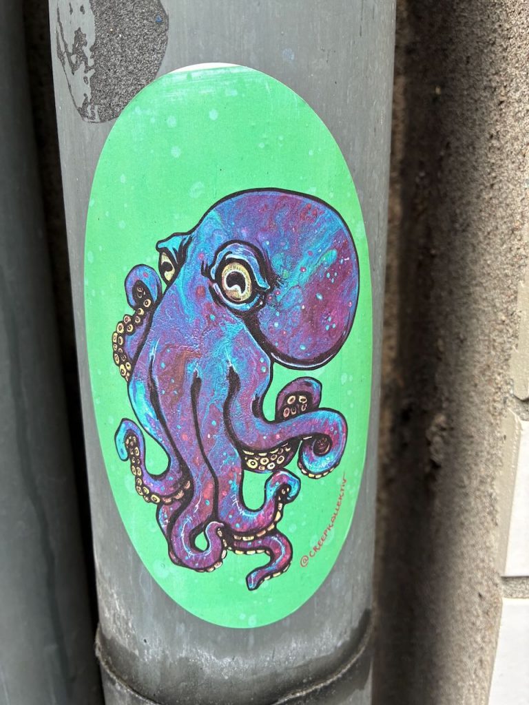 Ovaler Sticker auf grünem Grund mit einer detaillierten, lila-blauen Zeichnung eines Oktopus.