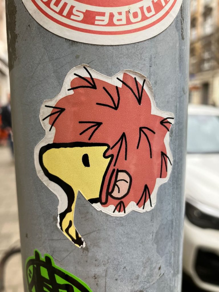 Ein Sticker halb abgerissen. Motiv: Woodstook mit Pumuckl-Frisur