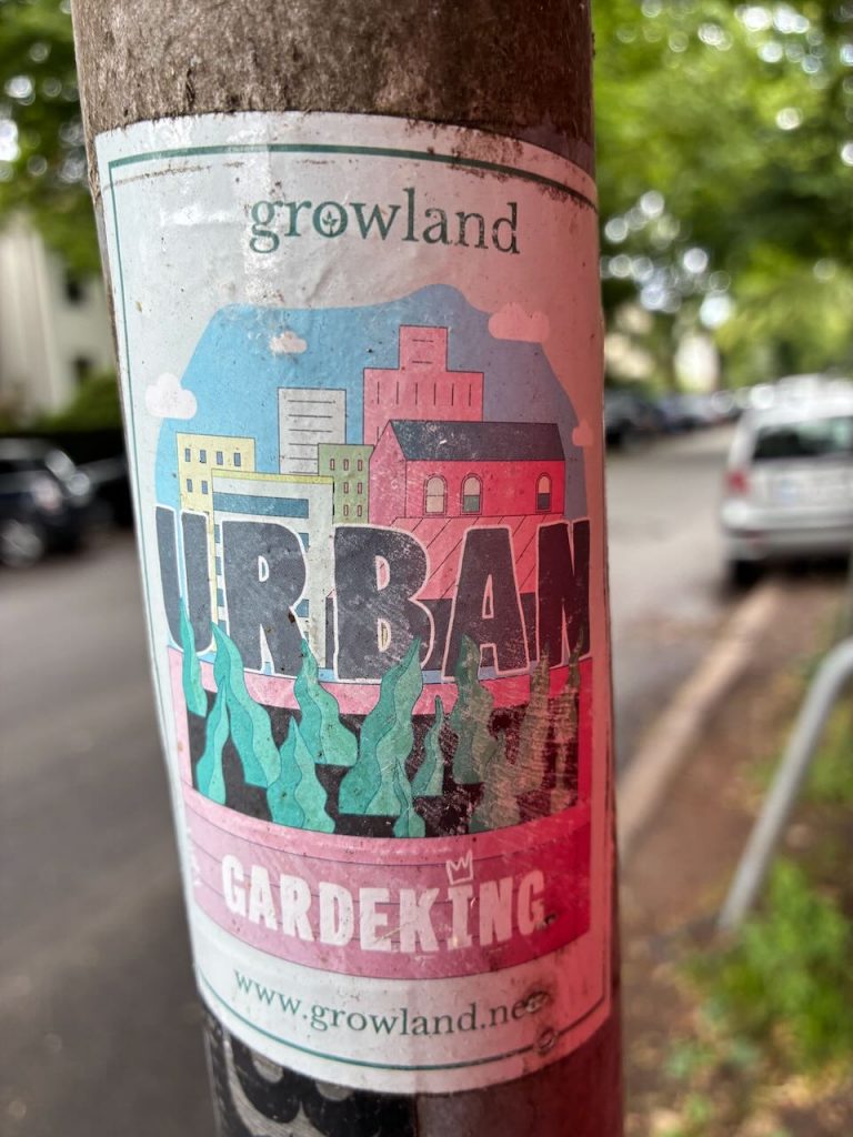 Rechteckiger Sticker mit der Aufschrift „growland“ oben. Darunter eine bunte Illustration von Häusern, Pflanzen und der Text „URBAN GARDEKING“. Unten steht die Webseite „www.growland.net“.