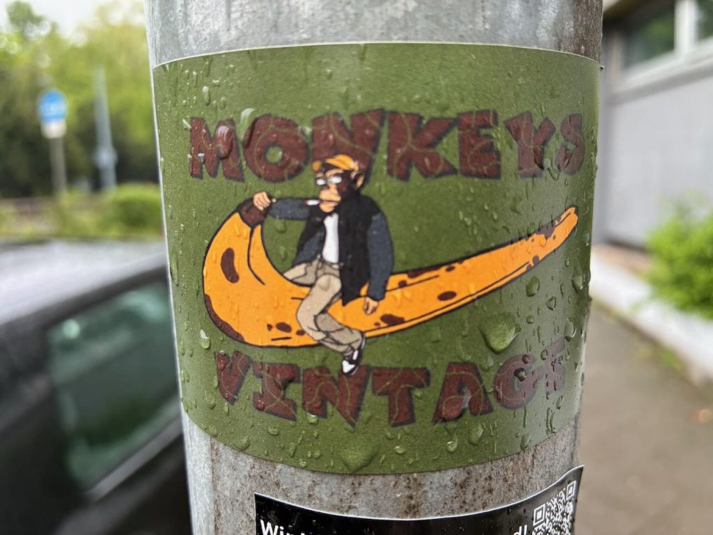 Grüner Sticker mit der Aufschrift „MONKEY’S VINTAGE“. In der Mitte sitzt eine gezeichnete Affenfigur mit Mütze und Jacke auf einer großen, gelben Banane.