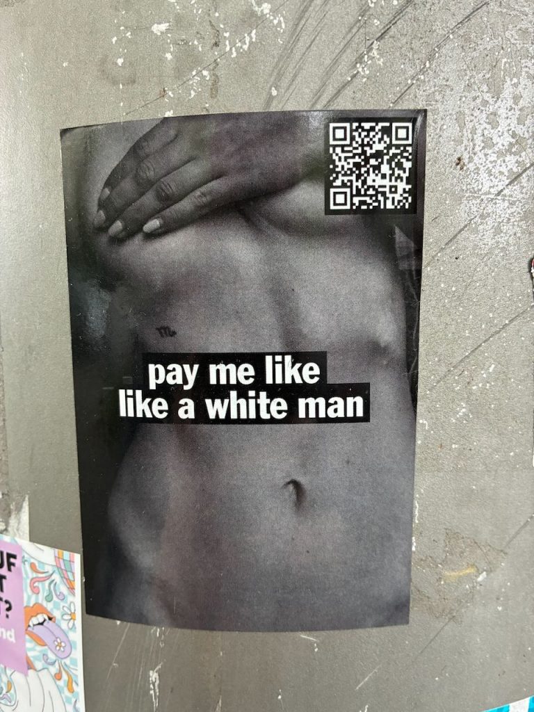 Stickerfoto eines nackten weiblichen Oberkörpers. Eine Hand liegt auf den Brüsten.
In der Mitte der Schriftzug: "pay me like a white man"