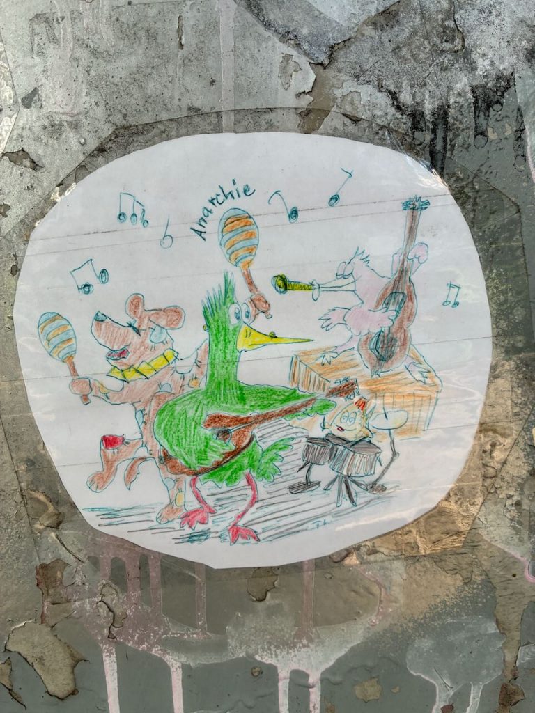 Ein handgezeichnetes Bild zeigt verschiedene Tiere als Musikband: Ein grüner Vogel mit Gitarre, ein Hund mit Schellen, eine Katze am Kontrabass und eine Trommel spielende Figur. Noten schweben in der Luft, es steht „Anarchie“ dabei.