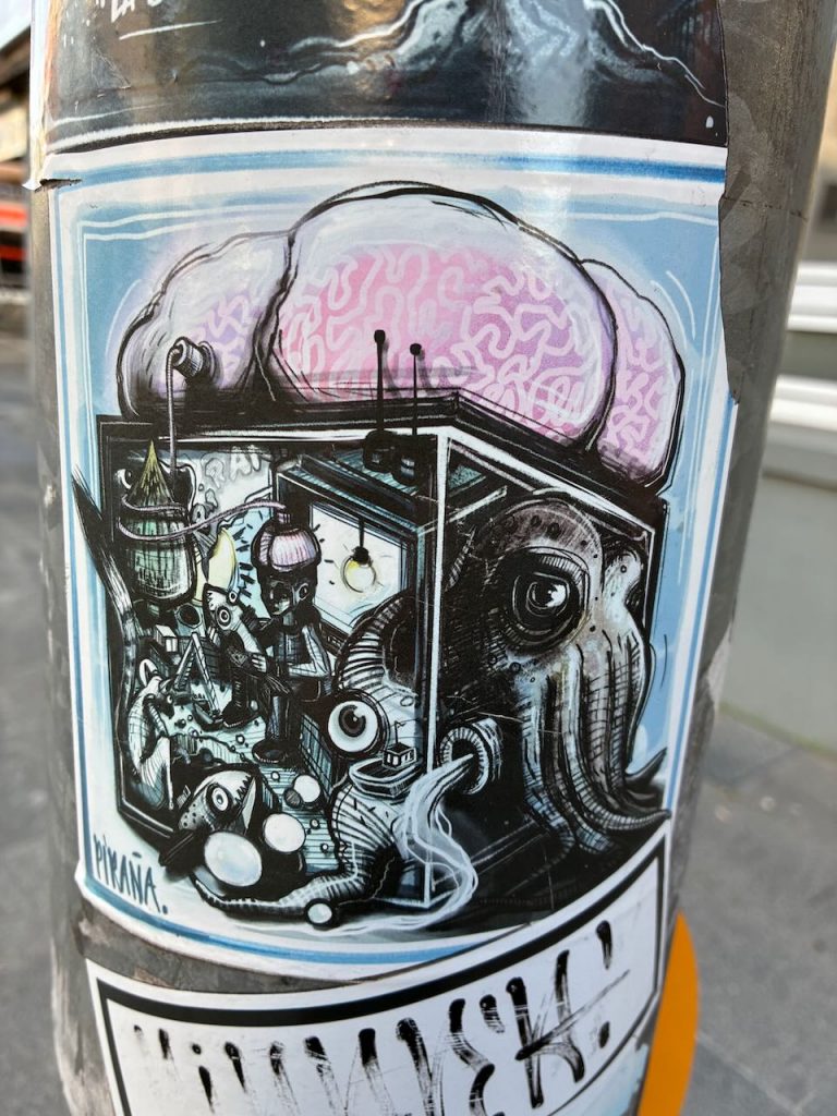 Ein komplexes, schwarzweißes Comicbild mit Tentakeln, einem großen Gehirn, technischen Details und vielen Augen, signiert mit „PIKAÑA“.