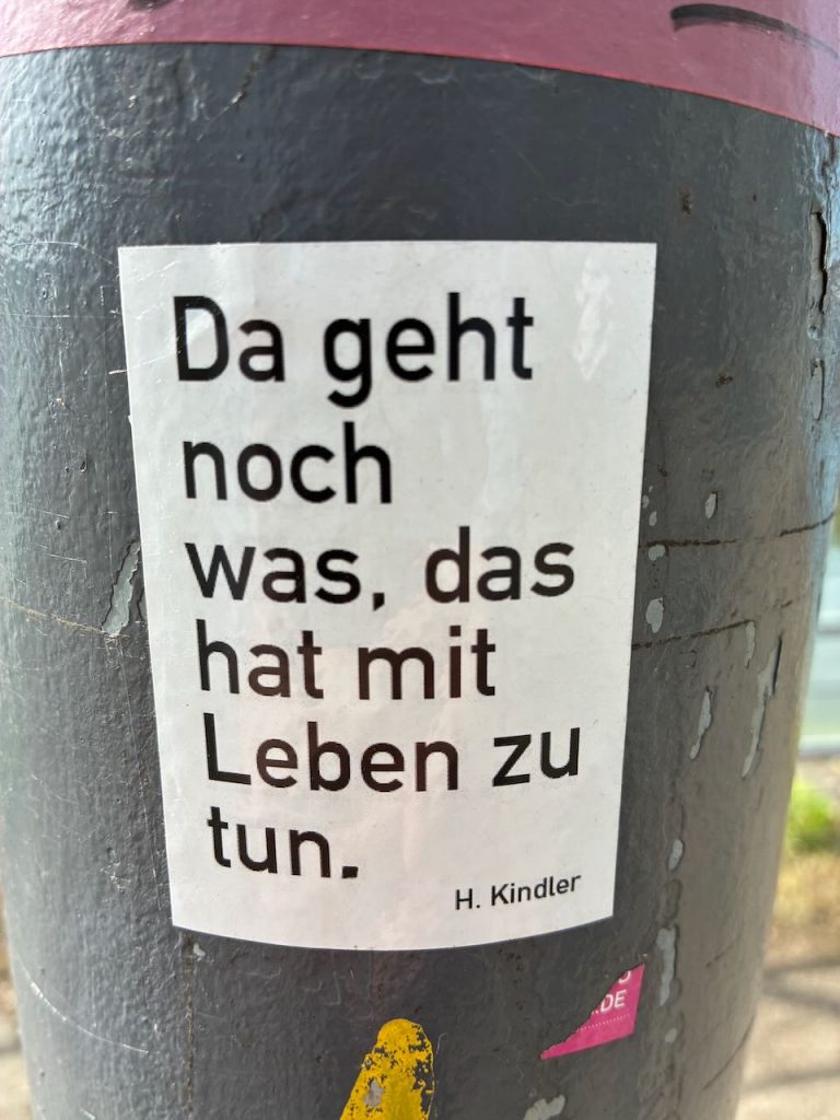 Weißer Aufkleber mit schwarzer Schrift auf grauem Untergrund: „Da geht noch was, das hat mit Leben zu tun.“ Darunter steht der Name „H. Kindler“.
