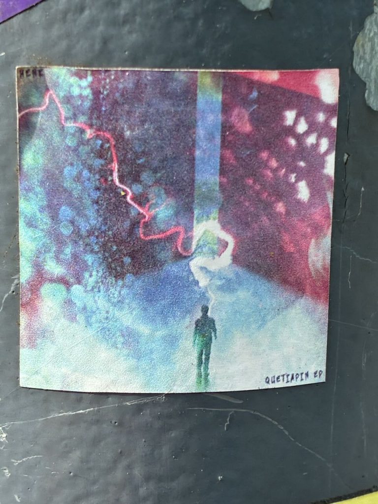 Rechteckiger Sticker mit bunten, abstrakten Mustern in Blau, Lila, Rot und Weiß. Unten steht eine kleine, schwarze Silhouette einer Person, darüber ein Lichtstrahl. Im Eck steht „QUETIAPIN EP“.
